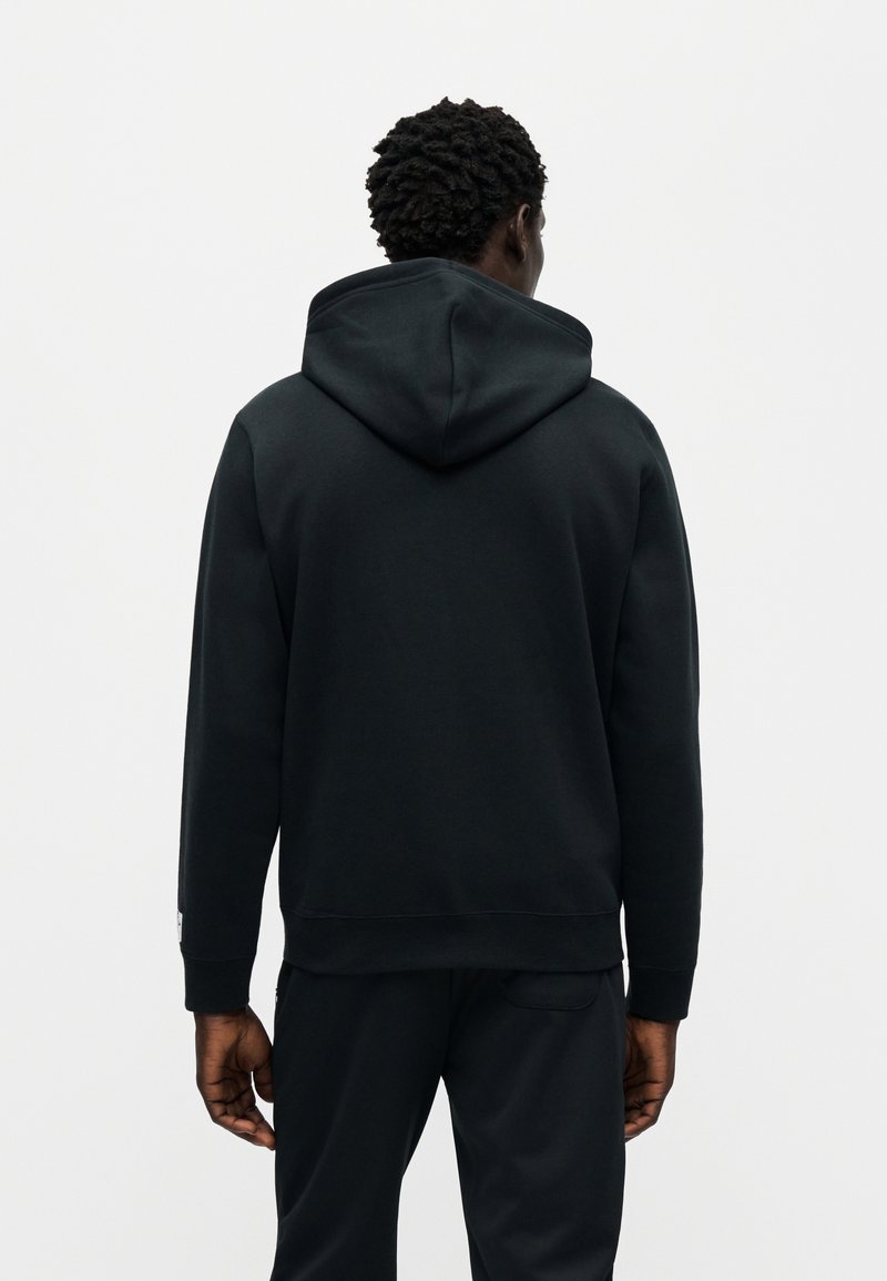 Sort hættetrøje med en afslappet pasform, der har et sømfrit rygdesign, ribstrikkede ærmekanter og en blød tekstur. Diskret branding på ærmet.