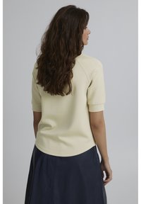 Lys gul kortærmet top med rund halsudskæring og raglanærmer, parret med en mørk navy nederdel. Glat tekstur, ensfarvet.