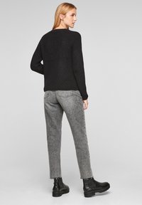 Un pull en tricot noir associé à un pantalon en denim droit gris, avec des ourlets effilochés et des bottines noires, vu de dos.