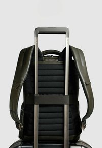 Mochila negra con secciones acolchadas, detalles verdes y un asa retráctil. Cuenta con correas de hombro ajustables y bolsillos con cremallera.