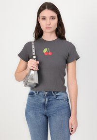 Szary prążkowany t-shirt z okrągłym dekoltem, ozdobiony haftem w czerwone wisienki, w połączeniu z niebieskimi dżinsami i metaliczną srebrną torebką.