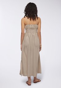 Abito maxi in tessuto beige con una finitura testurizzata, dotato di un corpetto arricciato e fessure laterali. Spalline sottili e vestibilità ampia.