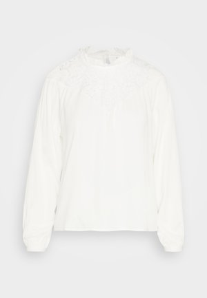 Blouse blanche à manches longues avec un col en dentelle haut, présentant des épaules froncées et une texture douce et lisse. Coupe droite avec une coupe décontractée.