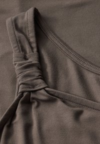 Brązowy top na ramiączkach z twisted strap. Gładka tekstura, elastyczny materiał oraz widoczne szwy wokół dekoltu i dolnej krawędzi.