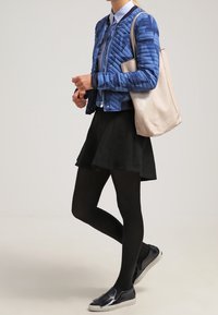 Gestepptes blaues Jacket, weißes Hemd mit Kragen, schwarzer Rock, schwarze Strumpfhosen und Slipper. Hellbeige Tote-Bag. Lässiges Ensemble.
