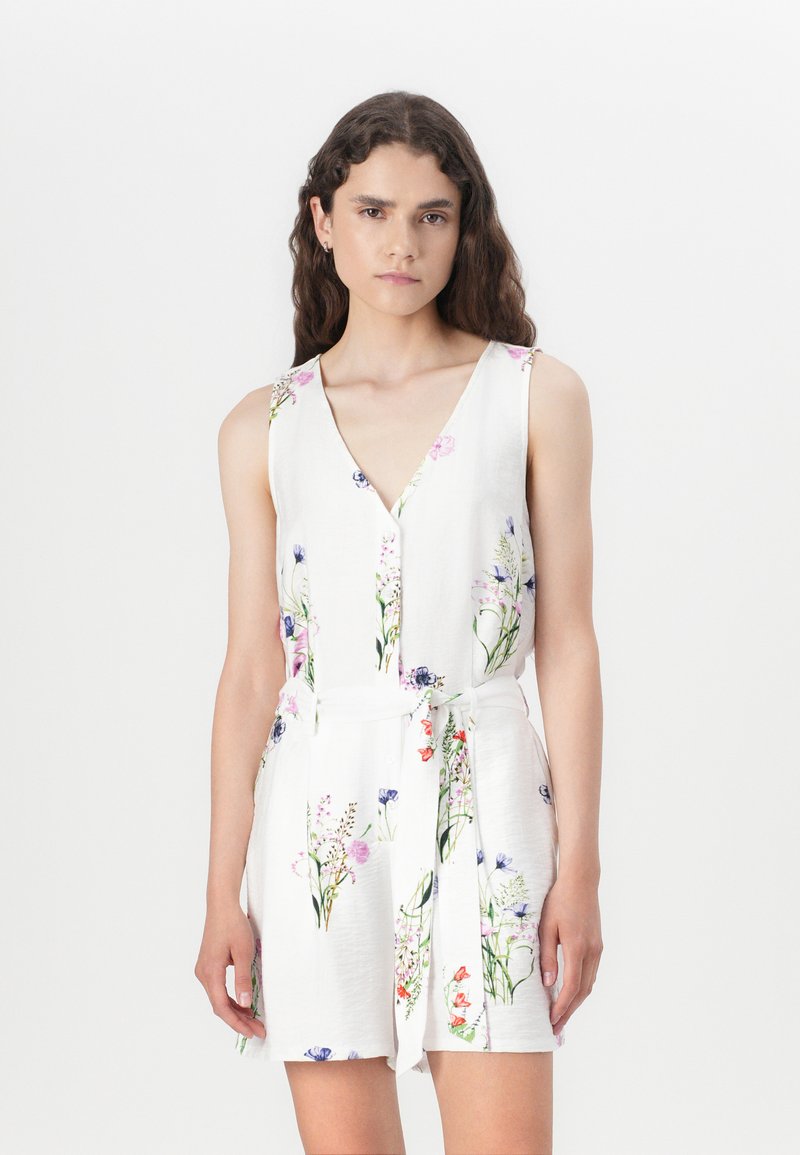 Salopette con stampa floreale in tessuto bianco, caratterizzata da un profondo scollo a V, design senza maniche, cintura regolabile con nodo e accenti di fiori colorati in tutto il capo.