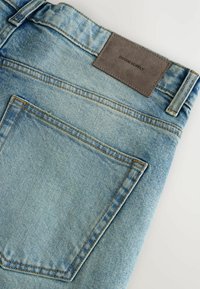 Világoskék farmernadrág, texturált felülettel, hátsó zsebbel, kontrasztos varrással és szürke bőr márkajelzéssel.