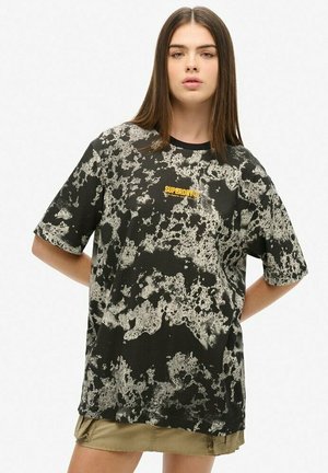 Czarna koszulka z białym wzorem plam, z żółtym logo "SUPERDRY". Krótkie rękawy, luźny krój, materiał bawełniany.