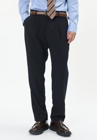 Tmavě modré plisované kalhoty se slim fit, doplněné hnědým koženým opaskem a lesklými hnědými botami. Viditelný detail texturované tkaniny.