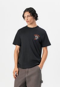 Schwarzes Baumwoll-T-Shirt mit kurzen Ärmeln und Rundhalsausschnitt. Auffälliges grafisches Design auf der Vorderseite in Orange, das das Gesicht eines Hundes zeigt.