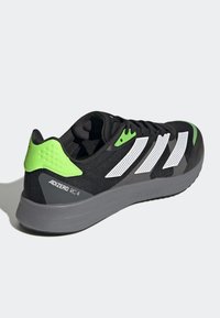 Scarpe da ginnastica nere con accenti verdi, strisce bianche, tomaia in tessuto, rete traspirante e suola grigia ammortizzata con etichetta "LIGHTSTRIKE".