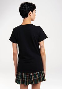 Black cotton t-shirt with short sleeves and a crew neckline, paired with a green plaid skirt featuring red and yellow accents.