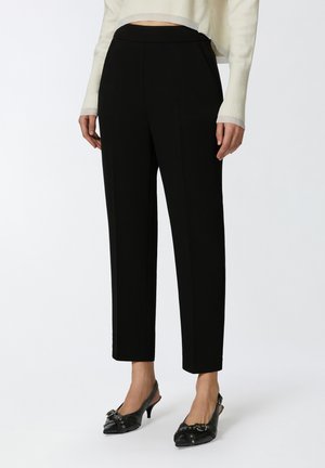 Pantalons noirs ajustés avec une coupe droite, présentant un devant plat et des poches latérales. Portés avec des escarpins noirs à bride arrière avec des accents décoratifs.