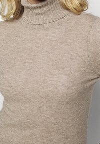 Beiger Rollkragenpullover aus weichem Strickmaterial, mit geripptem Kragen und Ärmeln. Figurbetontes Design mit glatter, gleichmäßiger Textur.