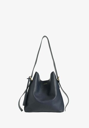 Sac en cuir noir à bandoulière avec une longue sangle ajustable, logo doré discret et pompon décoratif sur le côté, sur fond blanc.