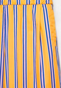 Tissu jaune avec des rayures verticales bleues, blanches et roses, avec une ceinture élastique et une fente latérale.