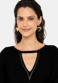 Top nero con scollatura a V caratterizzato da un dettaglio di borchie argento e orecchini a forma di cuore dorati. Tessuto morbido, design casual.