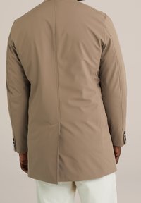 Béžový kabát s texturou a střih na míru, s rozparkem na zádech a manžetami na knoflíky. Měkký materiál s hladkým povrchem.