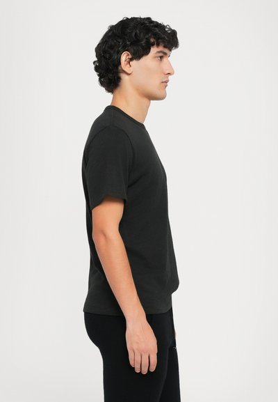 Camiseta negra de manga corta en tejido de algodón, con cuello redondo y un corte relajado. Textura suave, sin patrones ni adornos visibles.