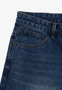 Ciemnoniebieskie dżinsy mają średnio wysoką talię, przednią kieszeń oraz pomarańczowe akcenty w stębnowaniu. Materiał ma teksturowane wykończenie.