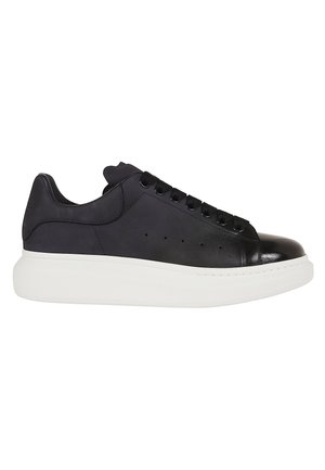 Sneakers basse nere con suola spessa bianca, lacci neri e fori di ventilazione traforati sul lato.