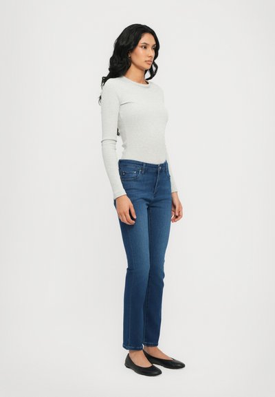 Lichtgrijze lange mouw top gecombineerd met donkerblauwe recht toelopende jeans, met een klassieke vijf-pocket ontwerp en zwarte platte schoenen.