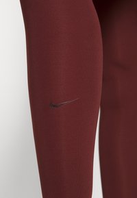 Maroon athletic leggings with a smooth texture, featuring a small black Nike logo on the left thigh.