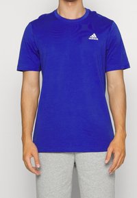 Sininen lyhythihainen T-paita, joka on valmistettu kevyestä materiaalista. Paita on pyöreällä kauluksella ja vasemmassa rintapielessä on valkoinen Adidas-logo.