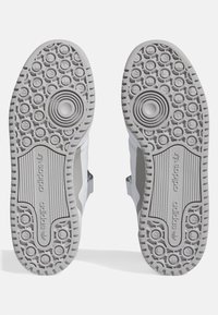 Adidas footwear soles in gray rubber, featuring textured circular patterns and deep grooves for traction. Subtle branding on the side.