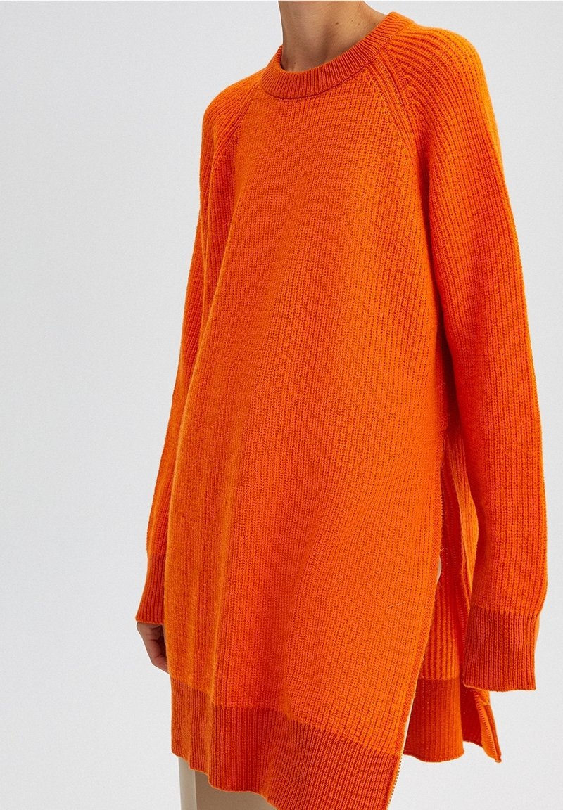 Luźny sweter z długim rękawem w żywym pomarańczowym kolorze, wykonany z dzianiny o fakturowanej powierzchni, z okrągłym dekoltem i bocznymi rozcięciami dla wygody.