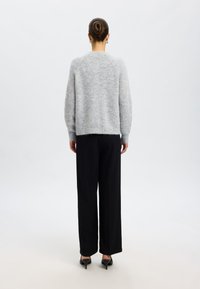 Light gray knit sweater with a relaxed fit and dropped shoulders, paired with black wide-leg trousers and black heels. Smooth texture.
