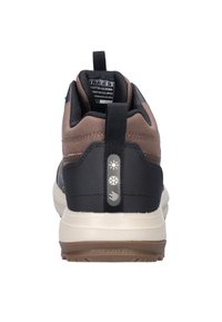 Bruine en zwarte Skechers sneaker gezien van achteren, met een trekband waarop zon-, sneeuwvlok- en regeniconen zijn afgebeeld, en een witte zool met loopvlak.