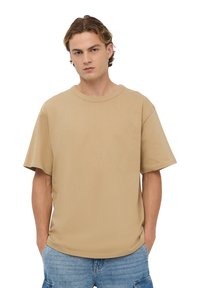 T-shirt beige a maniche corte in morbido cotone. Presenta un colletto rotondo, una vestibilità rilassata e spacchetti laterali per facilitare i movimenti.