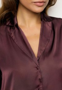 Camisa de seda burdeos con cuello clásico, botones frontales y textura suave, que enfatiza el material lujoso y el diseño elegante.