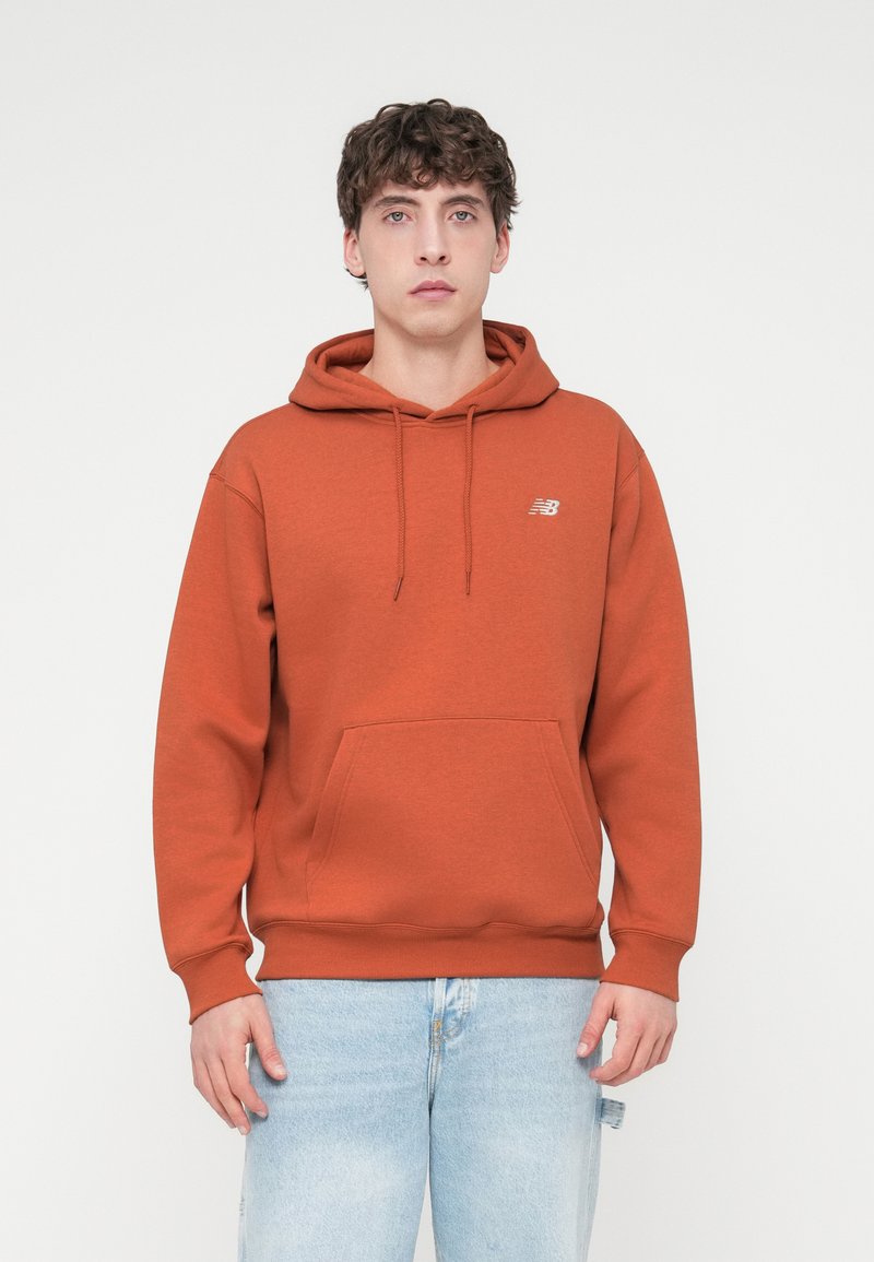 Kapuzensweatshirt in verbranntem Orange mit einer Kängurutasche vorne, gerippten Bündchen und einem kleinen Logo auf der Brust. Hergestellt aus weichem Stoff.