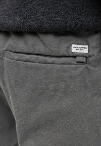 Graue Baumwoll-Sweatpants mit einem kleinen weißen Markenlabel "JACK & JONES EST. 1990" und einem Seitentaschen-Detail. Der Stoff wirkt weich und strukturiert.