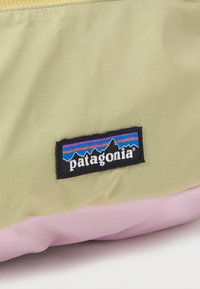 Μπεζ και ροζ ύφασμα με ένα ραμμένο μοτίβο λογότυπου Patagonia που απεικονίζει τη σιλουέτα ενός βουνού και πολύχρωμες ρίγες.