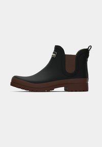 Zwarte rubberen enkelboot met een bruin elastisch zijpaneel en een gegraveerd logo. Beschikt over een gestructureerde zool voor grip en een aantrekhaak voor gemakkelijk aan- en uittrekken.