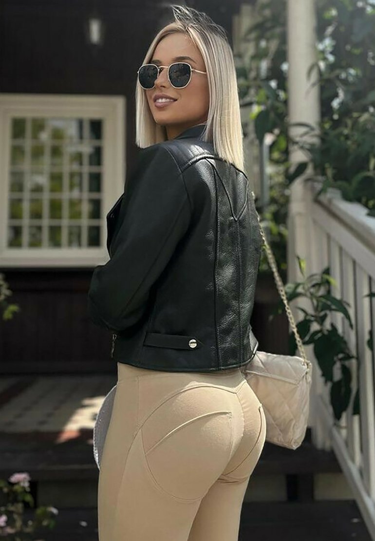 Giacca di pelle nera con accessori in argento, pantaloni beige a vita alta con evidenti dettagli di cuciture curve e una piccola borsa trapuntata.