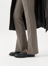 Black leather loafers with a smooth texture and sleek design, worn with light gray, tailored pants featuring a subtle ribbed pattern.