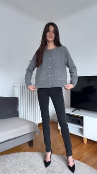Grå kort tröja med silverknappar och framfickor, kombinerad med svarta tajta jeans med en sidodetalj av strass och svarta klackar.