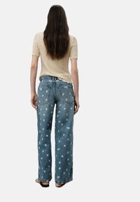 Ljust beige stickad topp med korta ärmar, kombinerad med ljusblå denimjeans med utspridd vit blommönstring och en avslappnad passform.