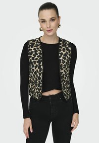 Prsluk s leopard uzorkom s crnim obrubom, bez rukava, teksturirana tkanina. Nositi preko uskog crnog rebrastog majice i uparen s crnim trapericama.