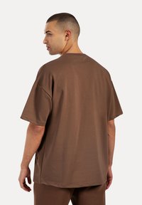 Camiseta oversized marrón hecha de tejido suave, con cuello redondo, mangas cortas y dobladillo recto. Sin patrones o acentos notables.