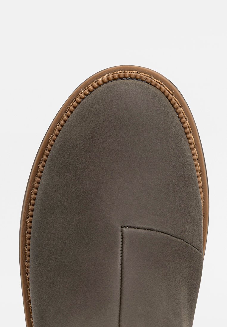 Close-up van de voorkant van een bruine leren schoen met gedetailleerde stiksels langs de rand en een gladde matte afwerking op de bovenkant.