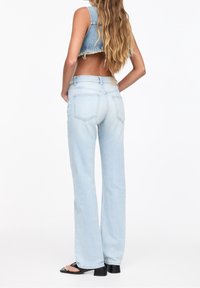 Jeans de mezclilla en tono claro, con corte acampanado, cintura media, bolsillos traseros y una superficie texturizada, combinados con un chaleco de mezclilla corto.