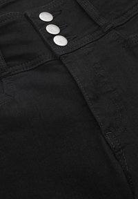 Mustat farkut, joissa on sileä pinta, korkea vyötärö ja kolme hopeista metallipainiketta edessä.