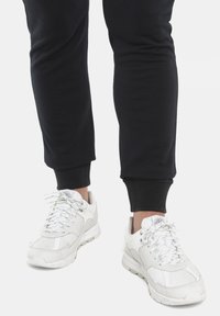 Sneaker sportive bianche con superfici testurizzate e pannelli in rete, abbinate a pantaloni da allenamento neri a gamba stretta con polsini elasticizzati.