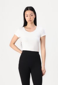 Witte t-shirt met korte mouwen en een ronde halslijn, gedragen met zwarte hoogwaterleggings. De stof lijkt glad en aansluitend.