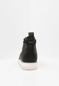 Black leather ankle boots with a textured finish, featuring a lace closure and a contrasting white sole, viewed from the back.